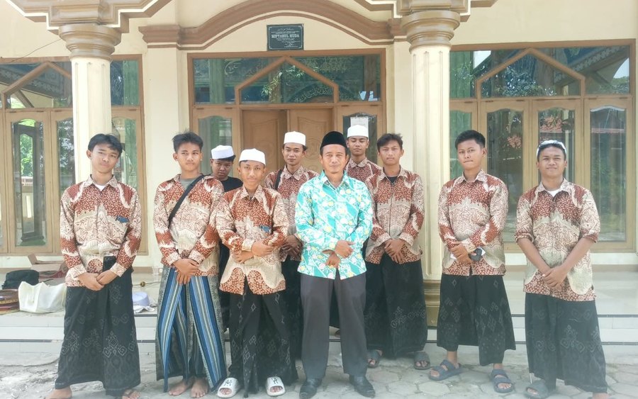 Foto grup hadroh Miftahul Huda Pakuning, para santri berkemeja batik dan berpeci putih berfoto bersama di depan bangunan pesantren