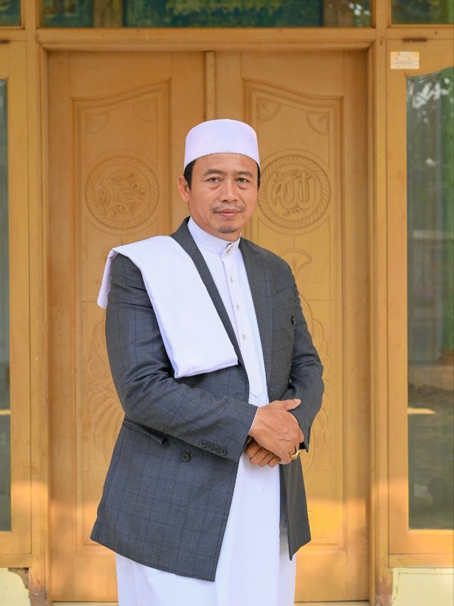 Ustadz Umar Abdullah, S.Ag., Pimpinan Pondok Pesantren Miftahul Huda Pakuning, mengenakan peci putih dan jas abu-abu